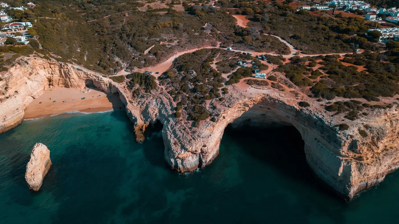 Stunning aerial view of rocky coastal cliffs with clear blue sea and sandy beach in a natural landscape.