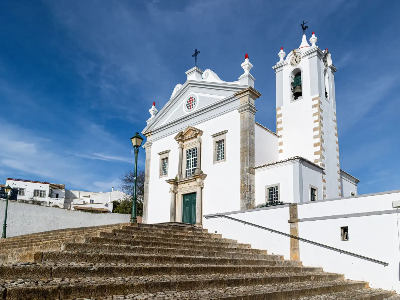 Historical white church facade with steps in Estoi, Faro, Portugal, under a clear blue sky.
