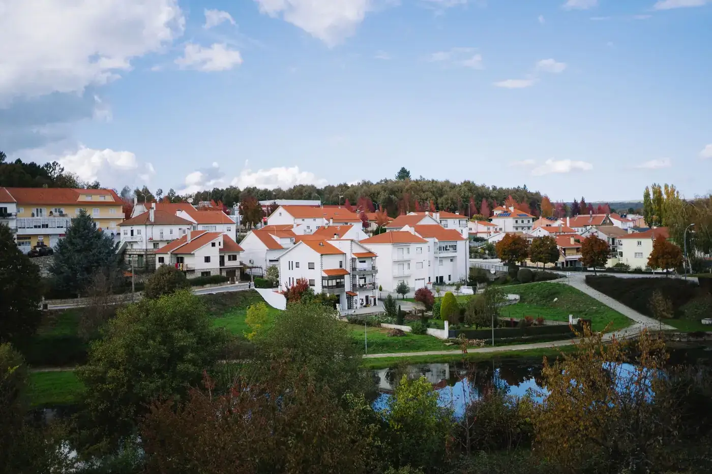 Charming suburban neighborhood with red rooftops and autumn foliage reflecting in a tranquil river.