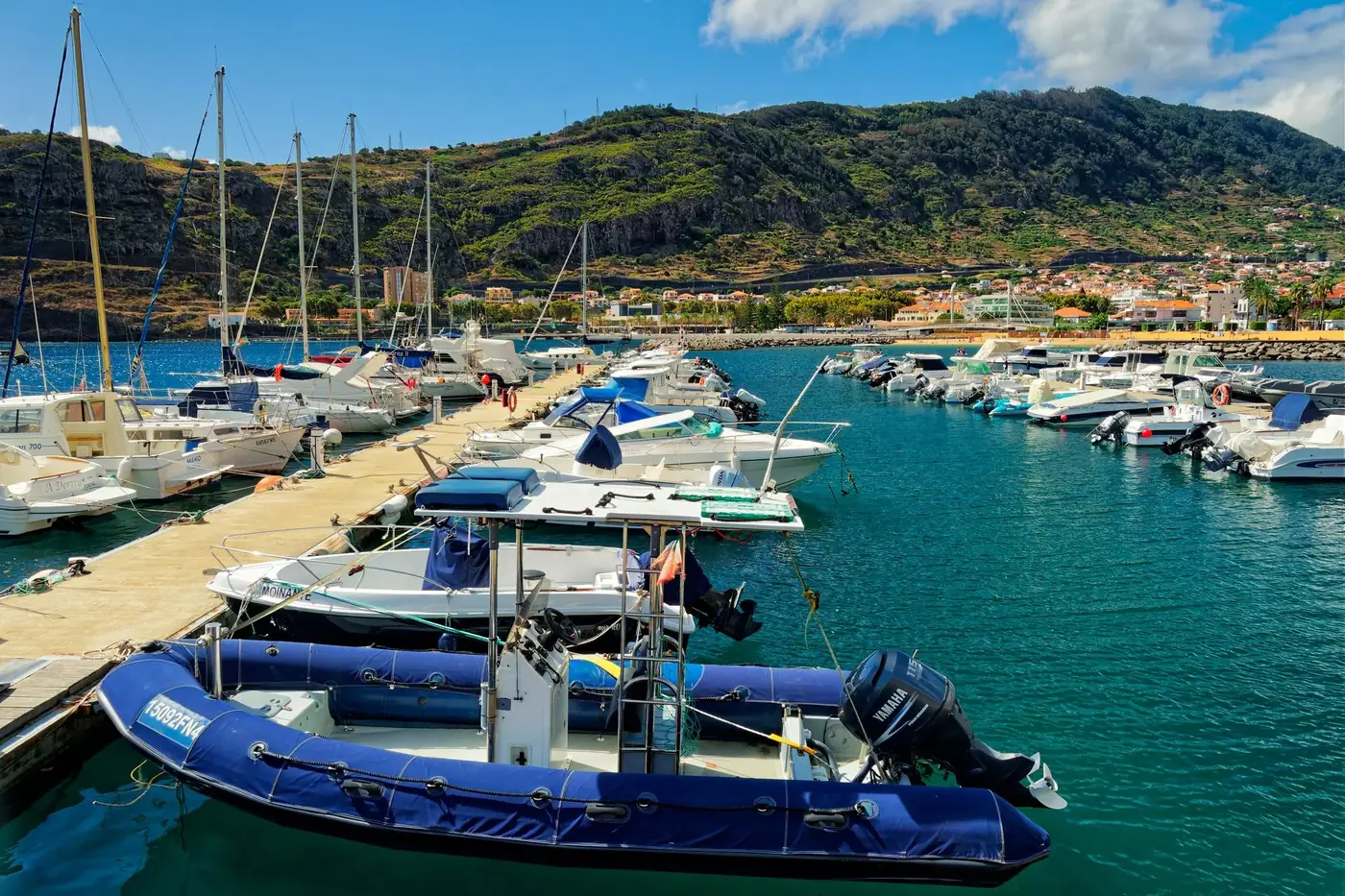 A tranquil marina with boats docked against scenic hillside views under a clear blue sky.