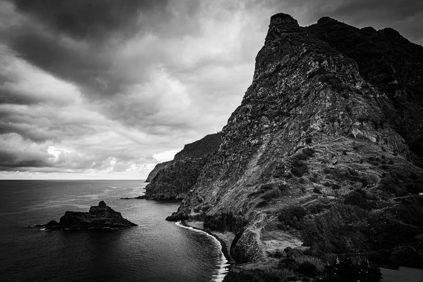 Black and white view of Madeira's dramatic cliffs and ocean under a moody sky.