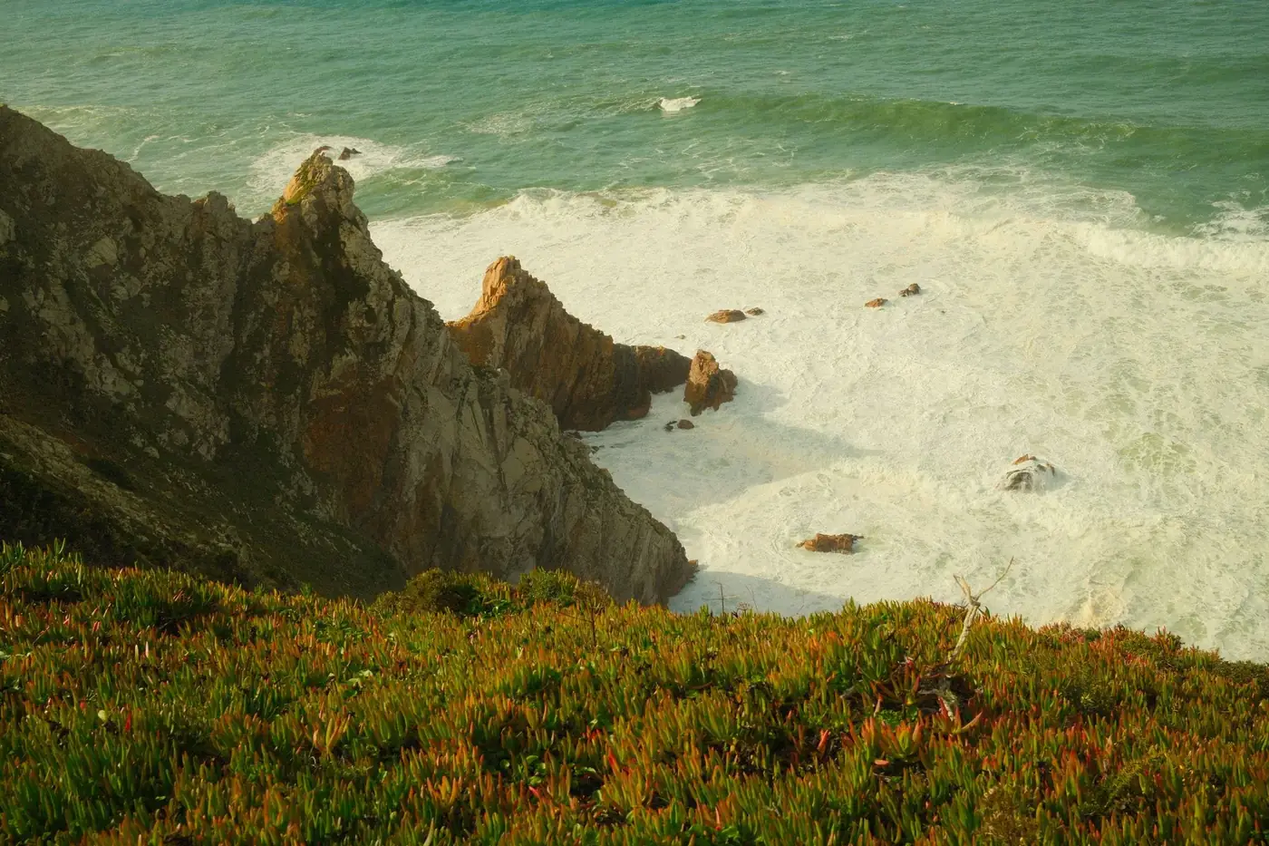 Sweeping view of rugged cliffs meeting crashing ocean waves in Colares, Portugal.