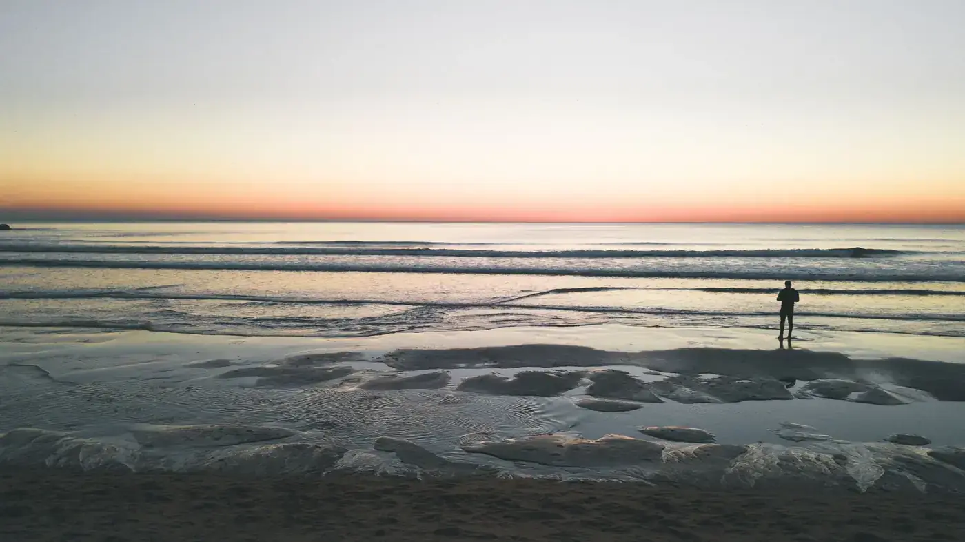 Lone figure on Costa da Caparica beach at sunrise, capturing a serene ocean view.