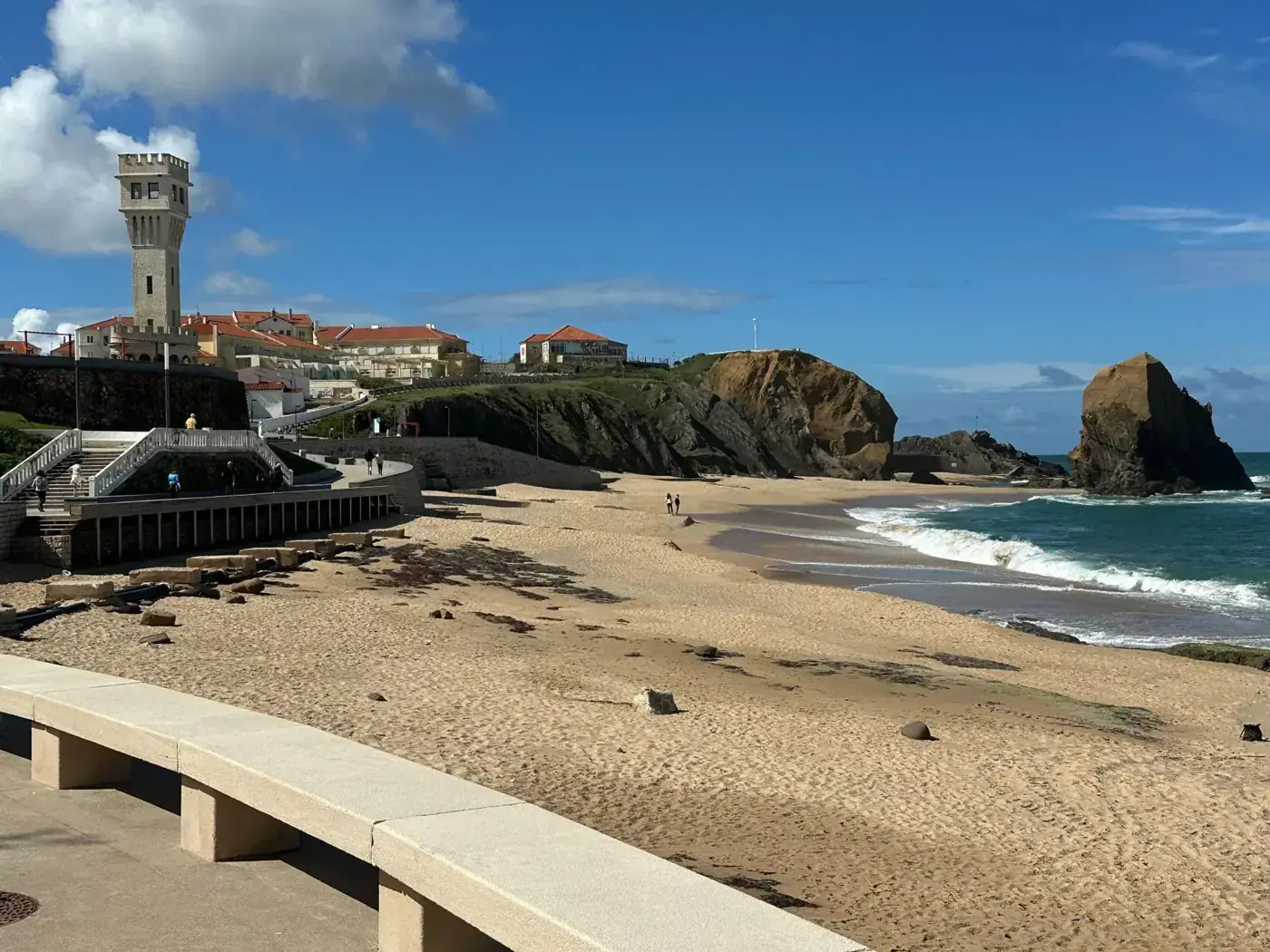 Sunny beach view of Praia de Santa Cruz with a scenic lighthouse and ocean waves.