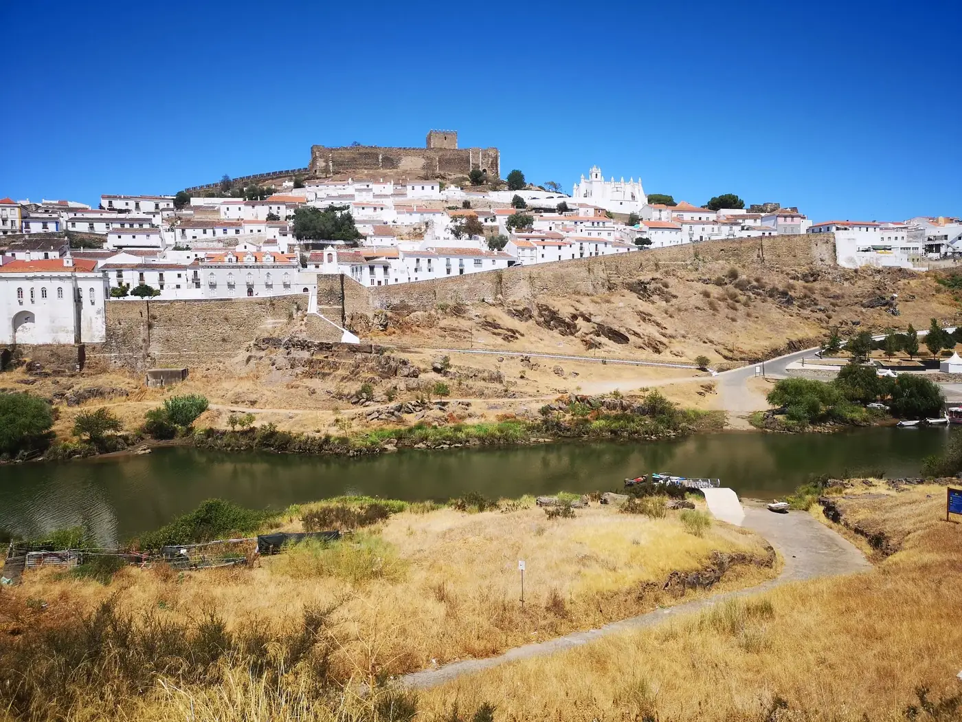 Picturesque Mértola town with its iconic castle and river Grande under a clear blue sky.