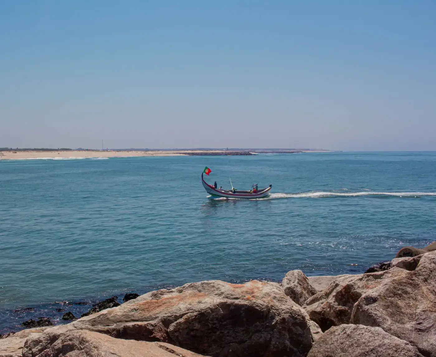 A traditional boat sails along the scenic rocky seashore on a bright summer day.