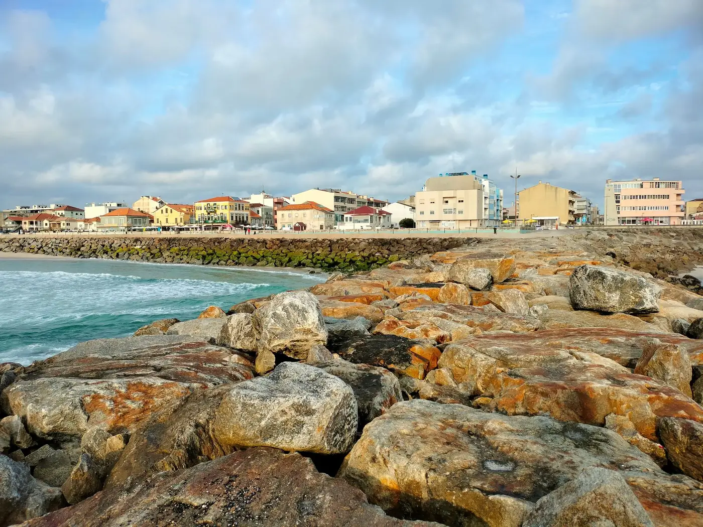 Picturesque rocky beach and cityscape under a cloudy sky.