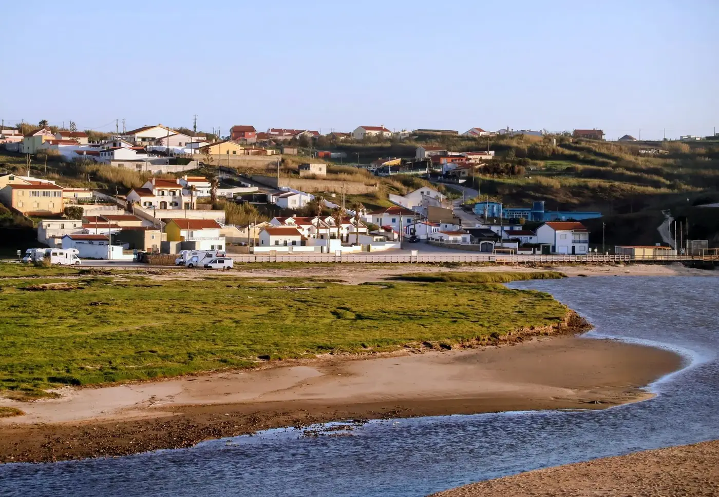 Quaint coastal village with rolling hills and vibrant green landscape under a clear sky.