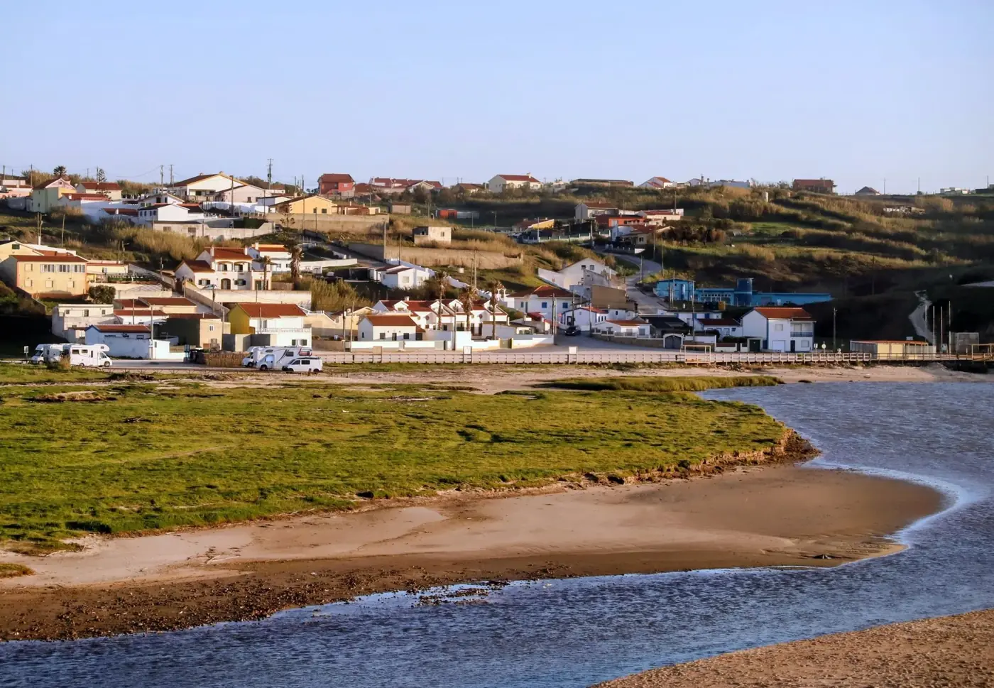 Quaint coastal village with rolling hills and vibrant green landscape under a clear sky.