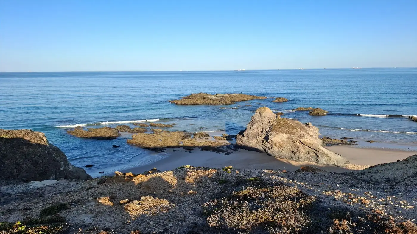 A serene view of the rocky coastline at Setúbal, Portugal, with clear blue skies and tranquil waters.