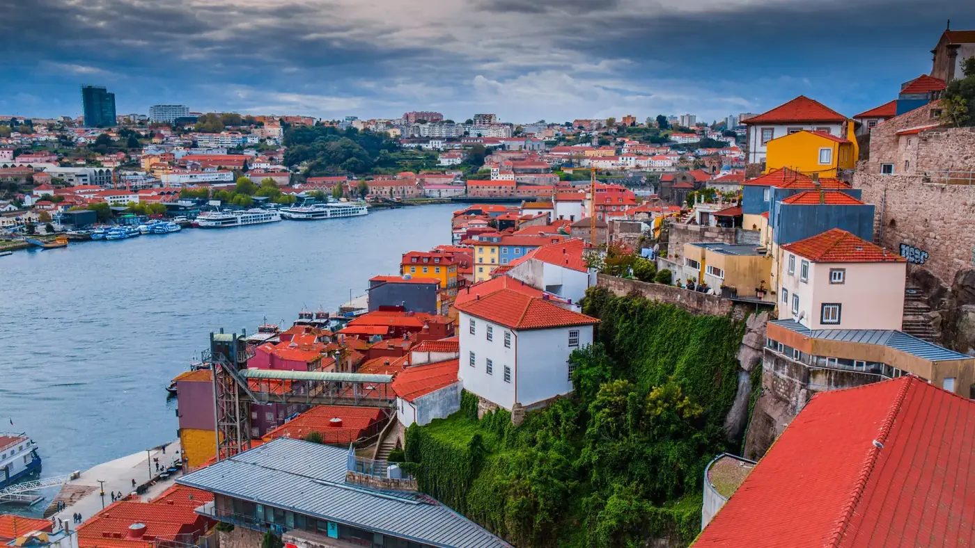 Scenic aerial view of Porto's vibrant riverside buildings along the Douro River under cloudy skies.