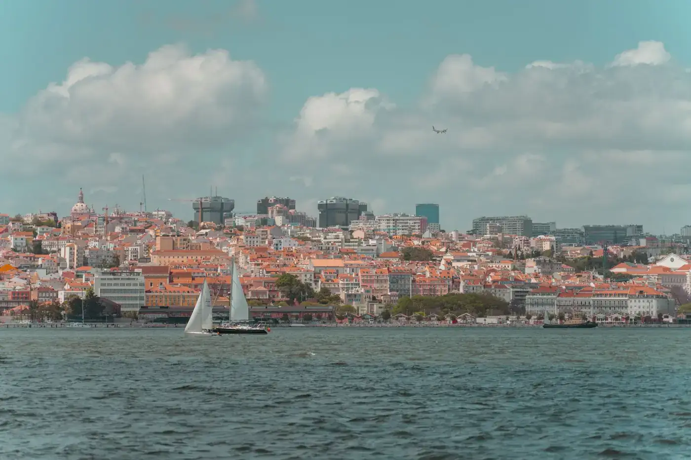 Peaceful scene of Lisbon's waterfront with sailboats and scenic city backdrop.
