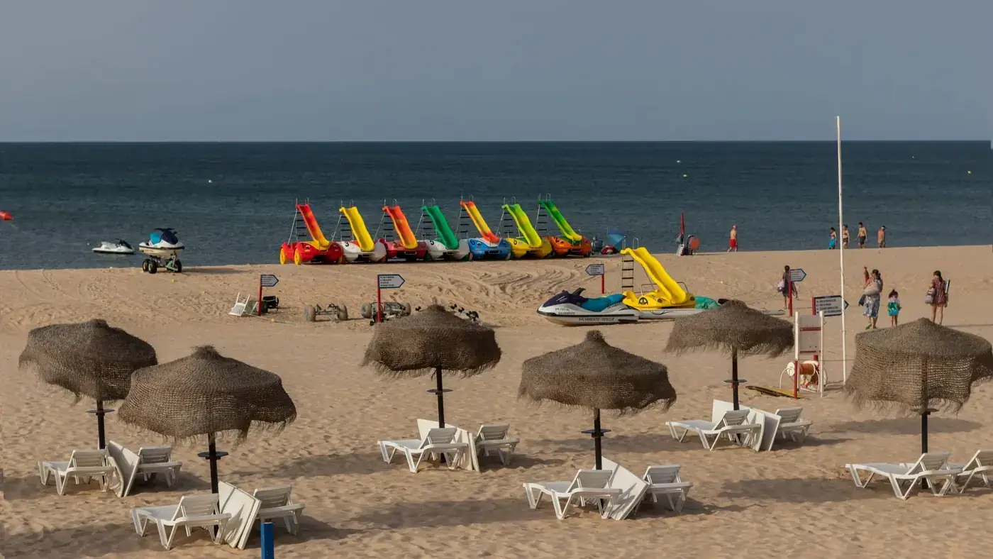Vibrant paddle boats and umbrellas on a sandy beach in Algarve, Portugal, under a clear sky.