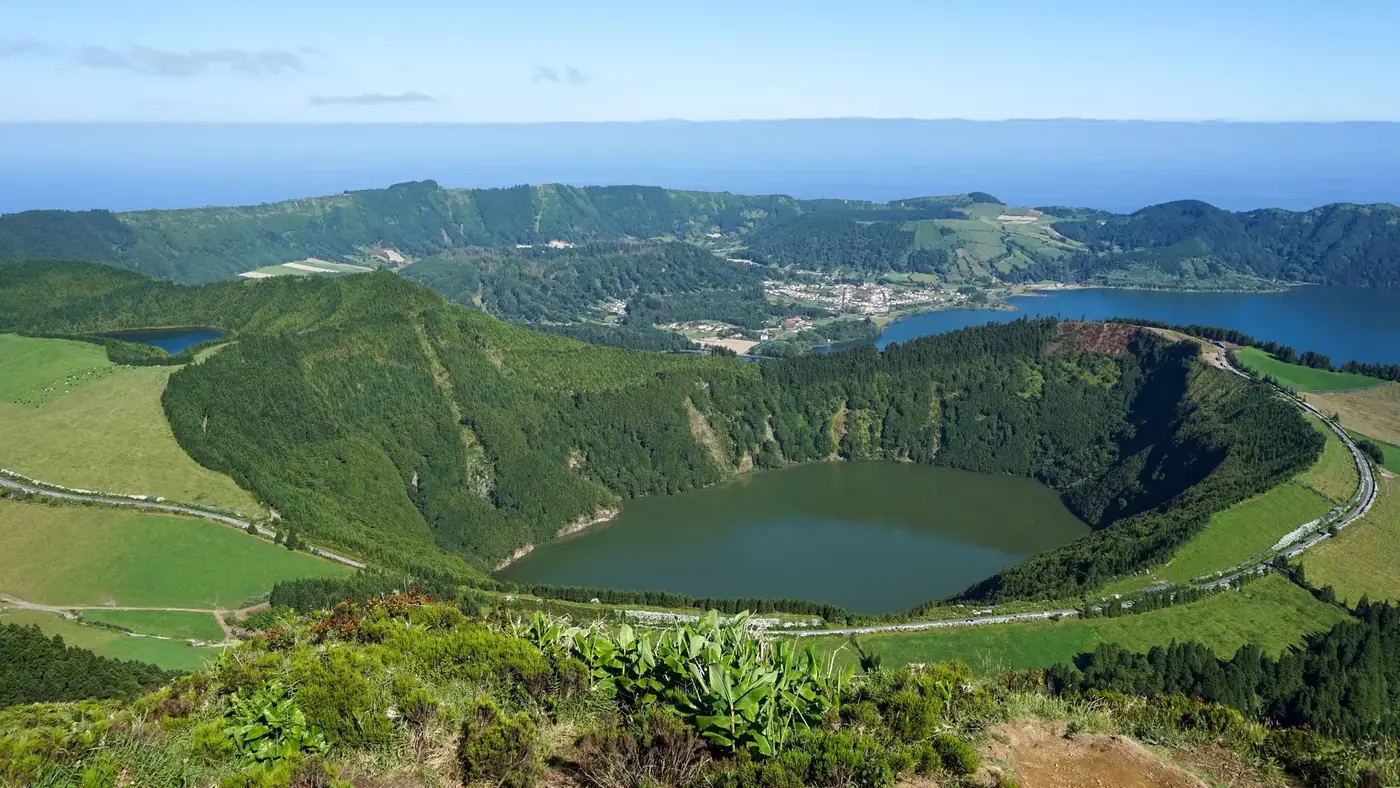 A stunning aerial view of a lush green landscape featuring a crater lake surrounded by hills and valleys.