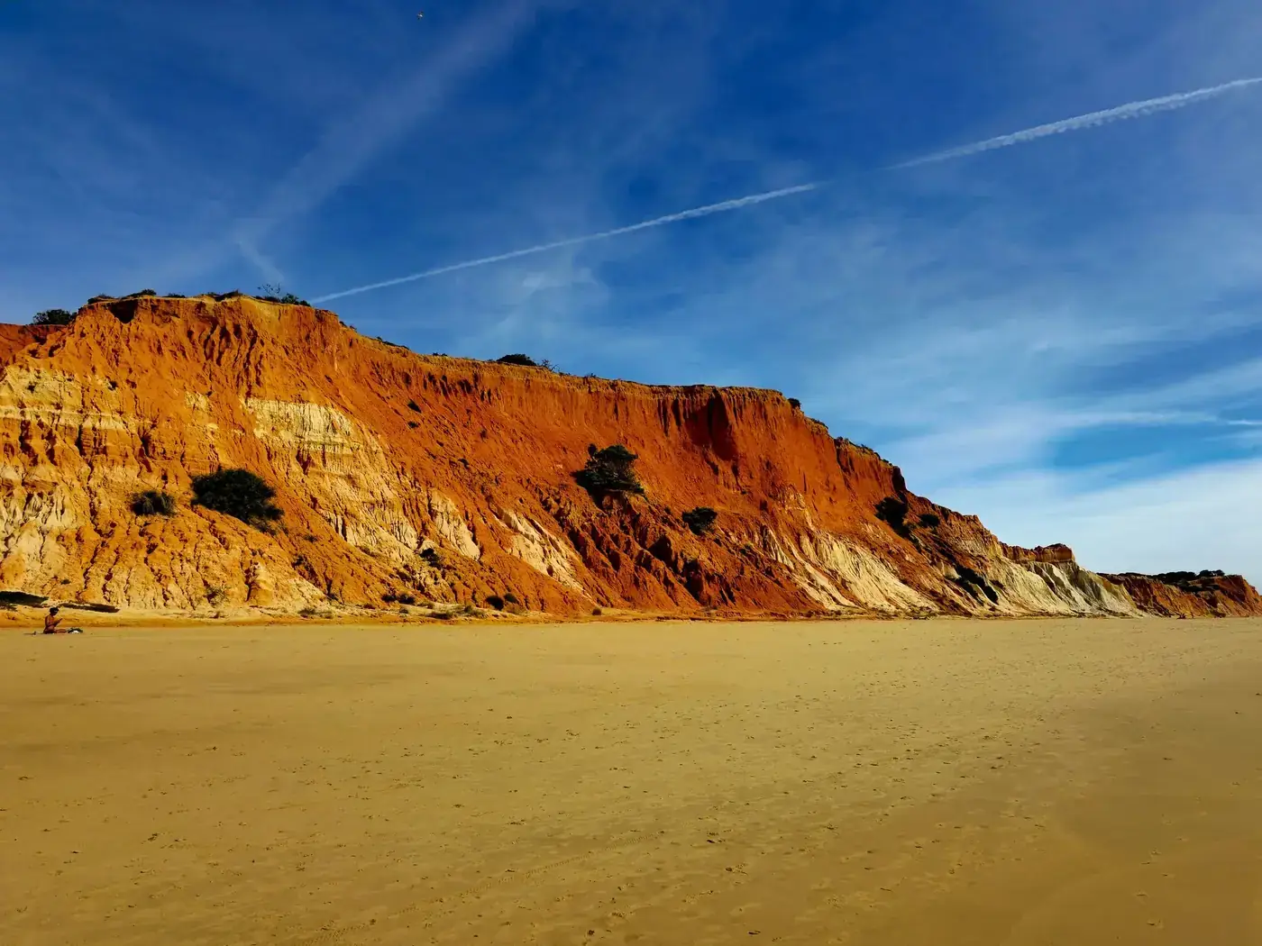 Breathtaking view of Praia da Falésia's red cliffs against a vibrant blue sky in Faro, Portugal.