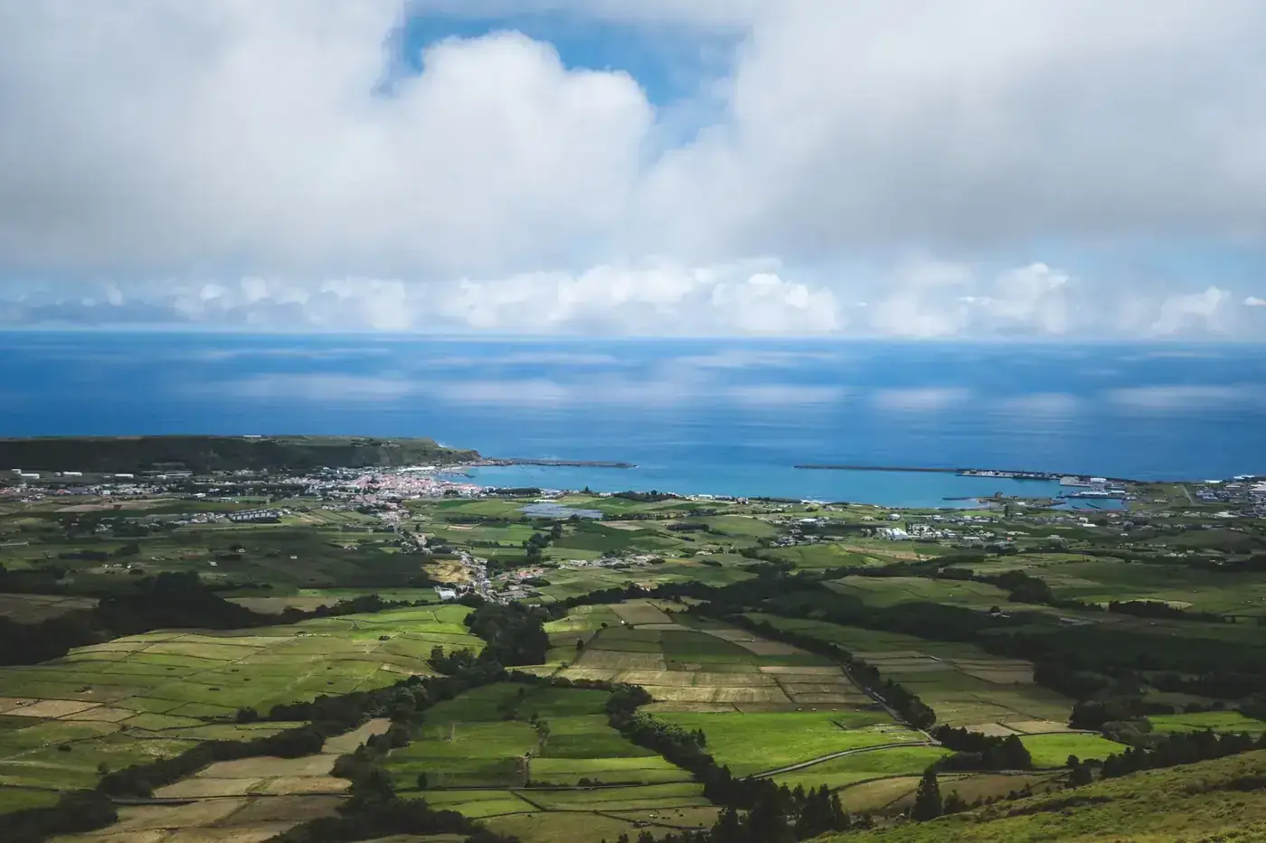 Stunning aerial view of coastal farmland leading to a vibrant ocean horizon on a clear day.
