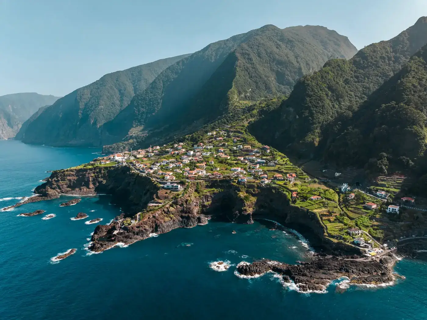 Scenic aerial view of a coastal village in Madeira, Portugal with lush green landscapes and rocky shores.