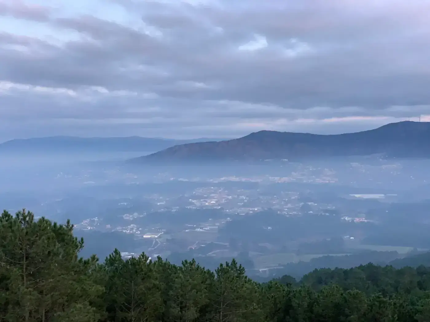 A serene, mist-covered view of the mountains and town of Vila Nova de Cerveira during the day.
