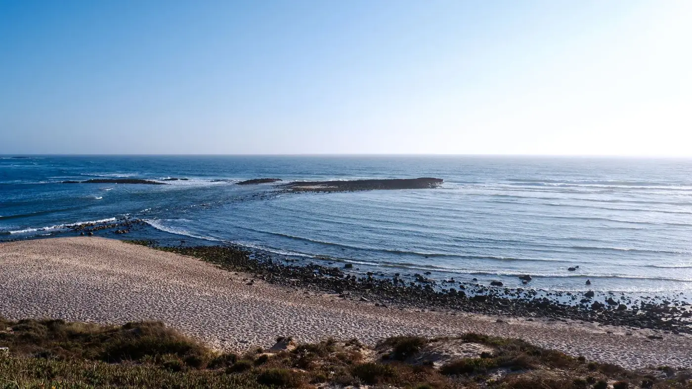 Serene coastal landscape at Vila Nova de Milfontes with blue ocean and rocky shore.